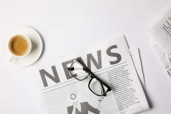 Flat lay with eyeglasses, cup of coffee and newspapers, on white table — Stock Photo