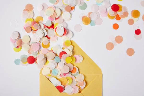 Vue de dessus des morceaux de confettis colorés et enveloppe jaune sur la surface blanche — Photo de stock