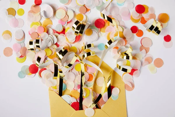 Elevated view of confetti pieces and yellow envelope on white surface — Stock Photo