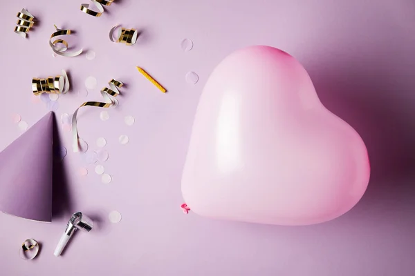 Vista superior de balão em forma de coração, chapéu de festa e peças de confete na superfície — Fotografia de Stock