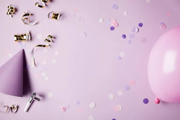 Vista superior de piezas de confeti, globo y sombrero de fiesta en la superficie violeta — Stock Photo