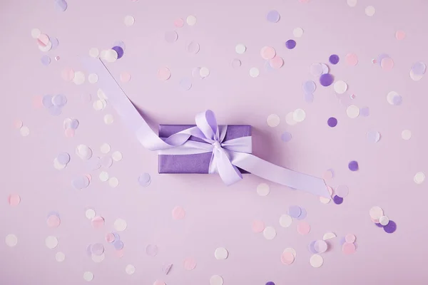 Vue de dessus d'une boîte cadeau violette et des morceaux de confettis sur la surface — Photo de stock