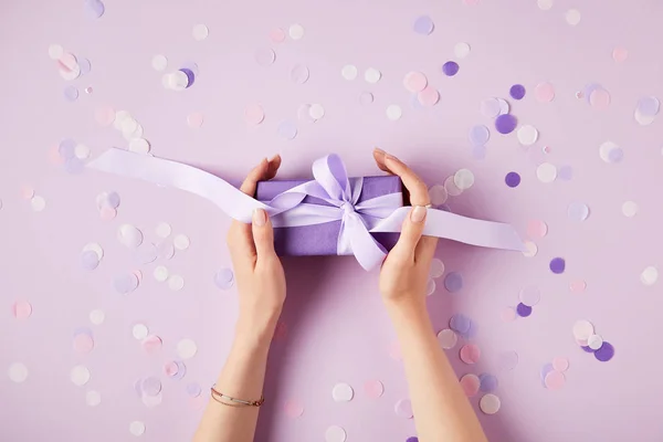 Cropped image of woman holding present box at table with confetti pieces — Stock Photo