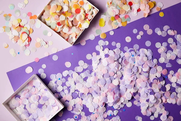 Vista elevada de piezas de confeti en cajas de papel y superficie violeta - foto de stock