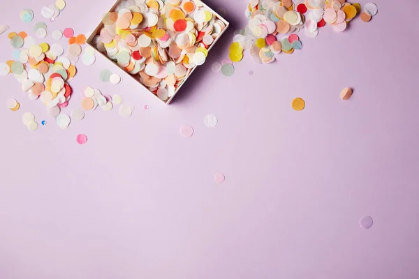 Vista superior de piezas de confeti en caja de papel y superficie violeta — Stock Photo