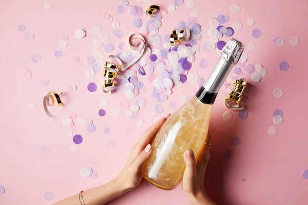 Imagen recortada de la mujer sosteniendo botella de champán por encima de confeti en la mesa de fiesta - foto de stock