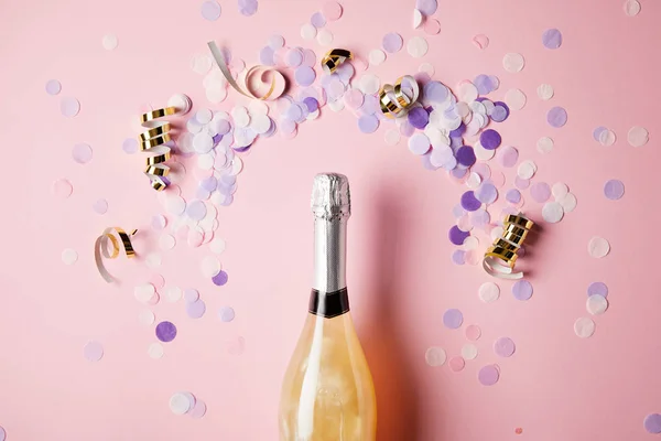 Vista superior de garrafa de champanhe e peças de confete na superfície rosa — Fotografia de Stock
