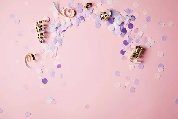 Vista elevada de piezas de confeti violeta en la superficie rosa - foto de stock