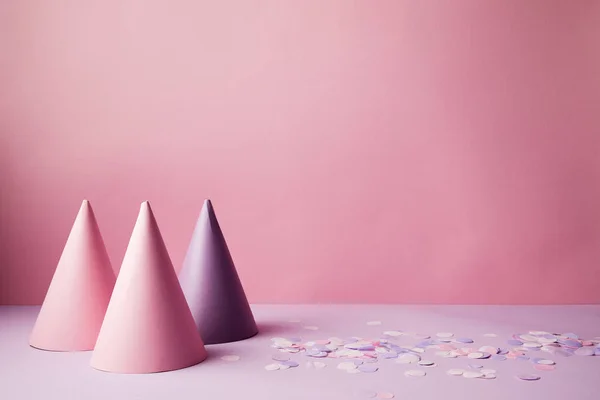 Pink and violet party hats and confetti pieces on violet surface — Stock Photo