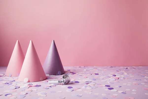 Chapeaux de fête roses et violets et morceaux de confettis sur dessus de table violet — Photo de stock