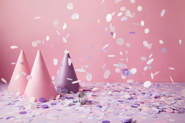 Sombreros de fiesta bajo la caída de piezas de confeti en la mesa violeta - foto de stock