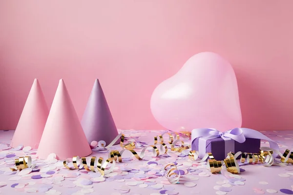 Globo en forma de corazón, sombreros de fiesta y presente en la mesa violeta - foto de stock