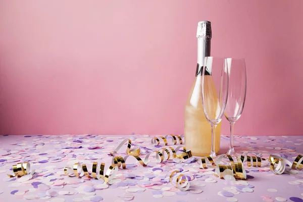 Botella de champán, vasos y piezas de confeti en la mesa violeta - foto de stock