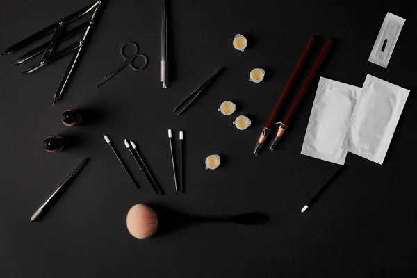 Вид кистей, карандашей, косметики и инструментов для перманентного макияжа на черном — стоковое фото