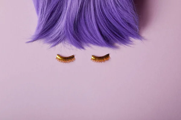 Vista superior de peluca violeta brillante y pestañas doradas falsas en púrpura - foto de stock