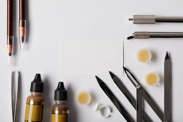 Top view of various tools and make up pencils for permanent makeup and blank card on white — Stock Photo