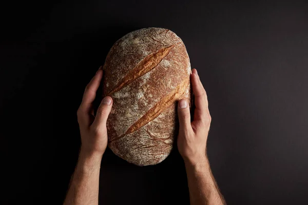 Colpo ritagliato di uomo che tiene il pane su un tavolo scuro — Foto stock