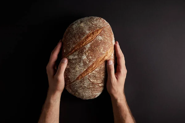 Cropped shot of man holding bread on dark tabletop — Stock Photo