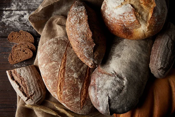 Високий вид на різні типи хліба, пшеницю та мішковину на дерев'яному столі, що покриває борошно — стокове фото