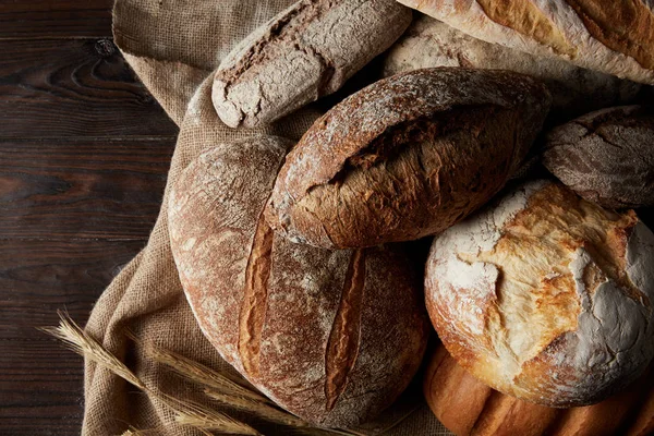 Draufsicht auf verschiedene Brotsorten, Weizen und Sacktuch auf Holztisch — Stockfoto