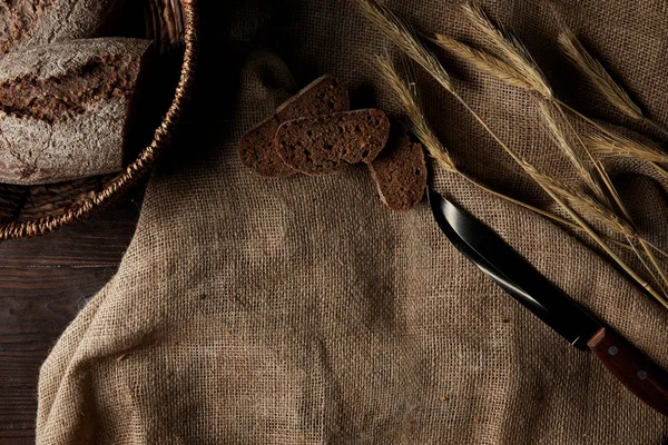 Vista superior de fatias de pão, saco, faca e cesta de pão de vime na mesa de madeira — Fotografia de Stock