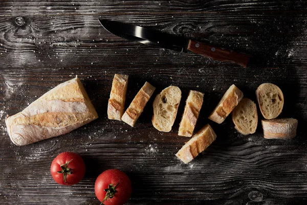 Vue de dessus des tranches de baguette, tomates et couteau sur table en bois recouverte de farine — Photo de stock