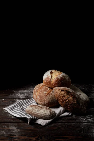 Nahaufnahme von verschiedenen Brotsorten und Sacktuch auf hölzerner Tischdecke mit Mehl isoliert auf schwarzem Hintergrund — Stockfoto