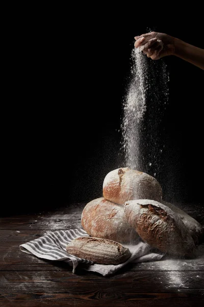 Vista parziale di panettiere femmina setacciare farina su vari tipi di pane su sacco isolato su sfondo nero — Foto stock