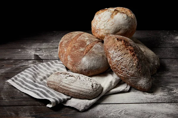 Closeup shot of various types of bread and sackcloth on wooden table covering by flour — Stock Photo