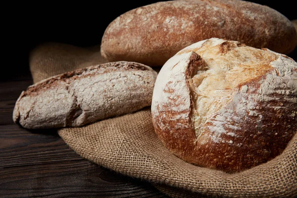 Close up image of various types of bread and sackcloth on wooden table — Stock Photo