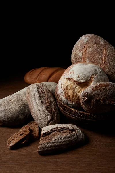 Nahaufnahme von verschiedenen Brotsorten und Weidenkorb auf Holztisch — Stockfoto
