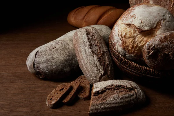 Close up image of various types of bread and wicker breadbasket on wooden table — Stock Photo