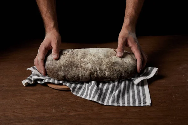 Cropped shot of male baker standing near table with bread, sackcloth and cutting board — Stock Photo