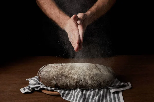 Tiro recortado de panadero macho aplaudiendo las manos con harina sobre el pan en el saco - foto de stock