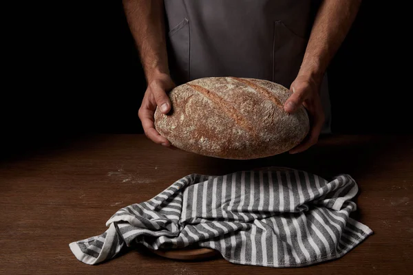 Teilansicht eines männlichen Bäckers in Schürze, der Brot über Holztisch hält — Stockfoto