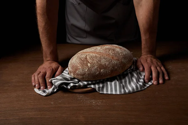 Imagem cortada de padeiro masculino em pé perto da mesa com pão e pano de saco — Fotografia de Stock