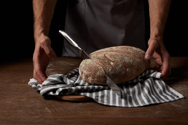 Tiro recortado de panadero macho de pie cerca de la mesa con pan, cuchillo y saco - foto de stock