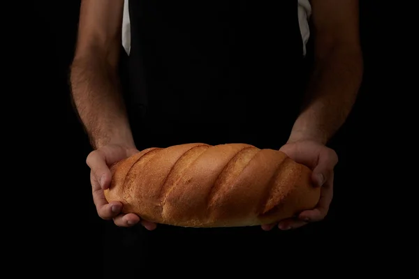 Cropped image of male baker in apron holding bread isolated on black background — Stock Photo