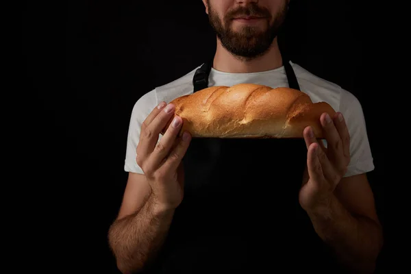 Corte tiro de padeiro macho em avental segurando pão isolado no fundo preto — Fotografia de Stock