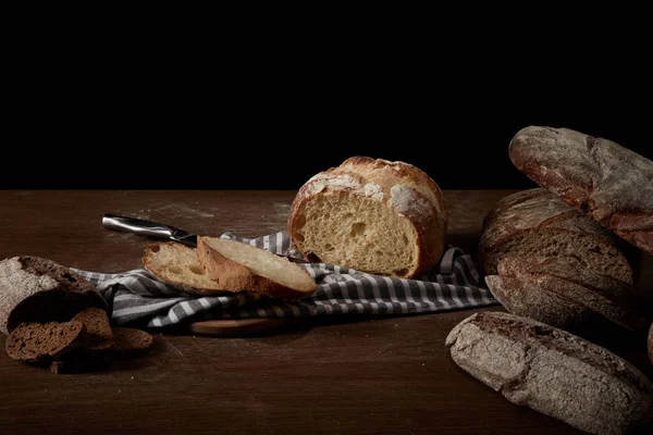 Closeup image of various types of bread, sackcloth, knife and cutting board on table — Stock Photo