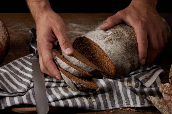 Vista parcial del panadero macho tomando rebanadas de pan en la mesa de madera con saco y cuchillo - foto de stock