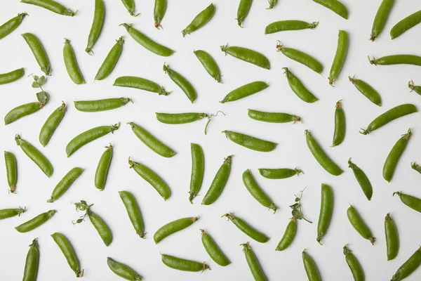 Vista superior de vainas de guisantes verdes derramadas sobre la superficie blanca - foto de stock