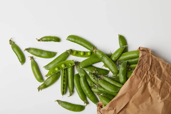 Top view of ripe pea pods spilled from paper bag on white surface — Stock Photo