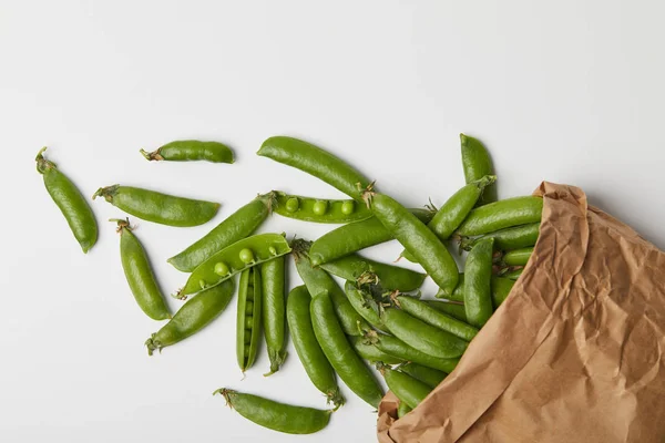 Vue du dessus des gousses de pois mûrs renversées du sac en papier sur la surface blanche — Photo de stock