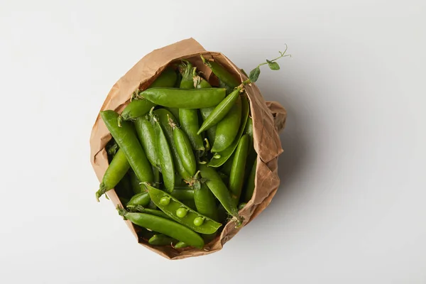 Vue du dessus des gousses de pois dans un sac en papier sur une surface blanche — Photo de stock