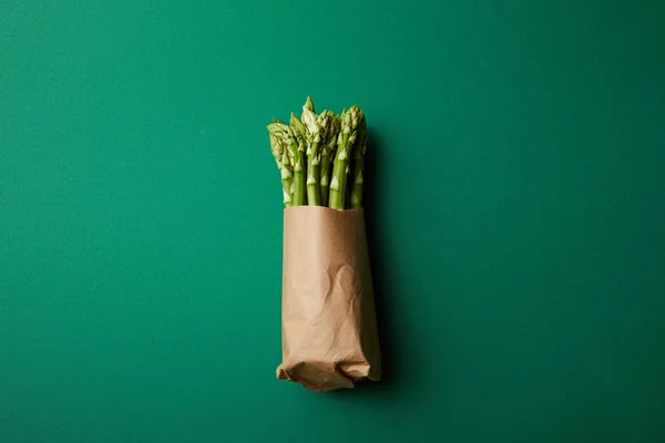 Vista superior del manojo de espárragos maduros cubiertos con papel kraft en la superficie verde - foto de stock