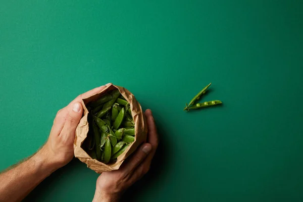 Cropped shot of man holding paper bag with pea pods on green surface — Stock Photo