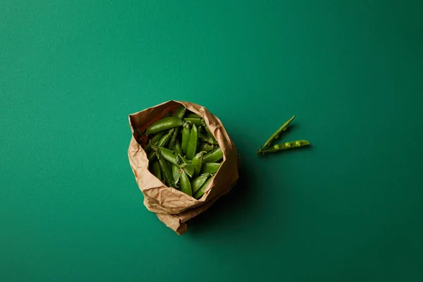 Vista superior do saco de papel com vagens de ervilha na superfície verde — Fotografia de Stock