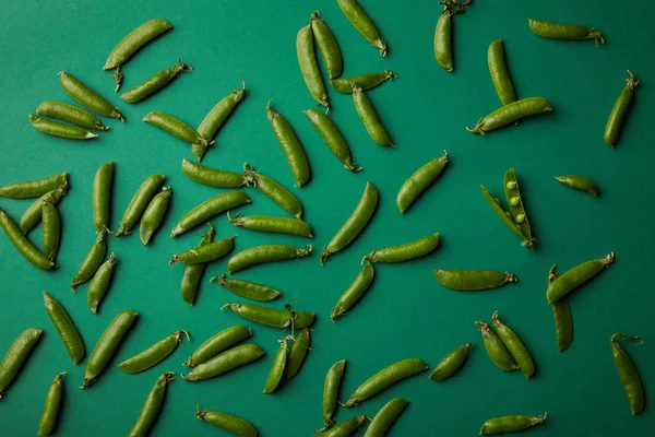 Vue de dessus des gousses de pois déversées sur la surface verte — Photo de stock