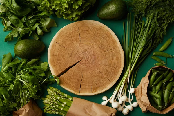 Vue de dessus de la coupe de bois entourée de divers légumes mûrs sur la surface verte — Photo de stock